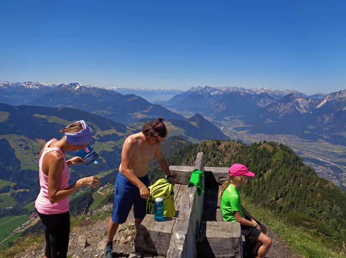 am benachbarten Westgipfel vier große Holzbänke aus einem Riesenstamm; Blick das Inntal hinauf auf Tuxer und Stubaier Alpen, rechts davon das Karwendel