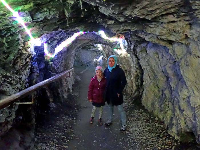 ein beleuchteter Tunnel leitet hinunter auf die Höhe des Ederspitz; Ronja und Fereshta am Ende eines Probestollens, der vor langer Zeit auf der Suche nach Gold in die Schluchtwand getrieben worden ist