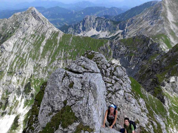 von einem grünen Absatz rechts der senkrechten Kante bis aufs Bandende (!) queren (Steinmänner) und auf der zweiten Rampe links zurück auf die Gratschneide; so erreicht man die schöne 6-m-Platte am oberen Gratteil